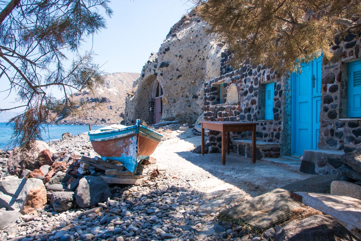 Thirassia - Bootsgaragen im Hafen Riva - altes Holzboot, Tisch und Türen im Felsen kombinieren sich zu einem perfekten Stilleben